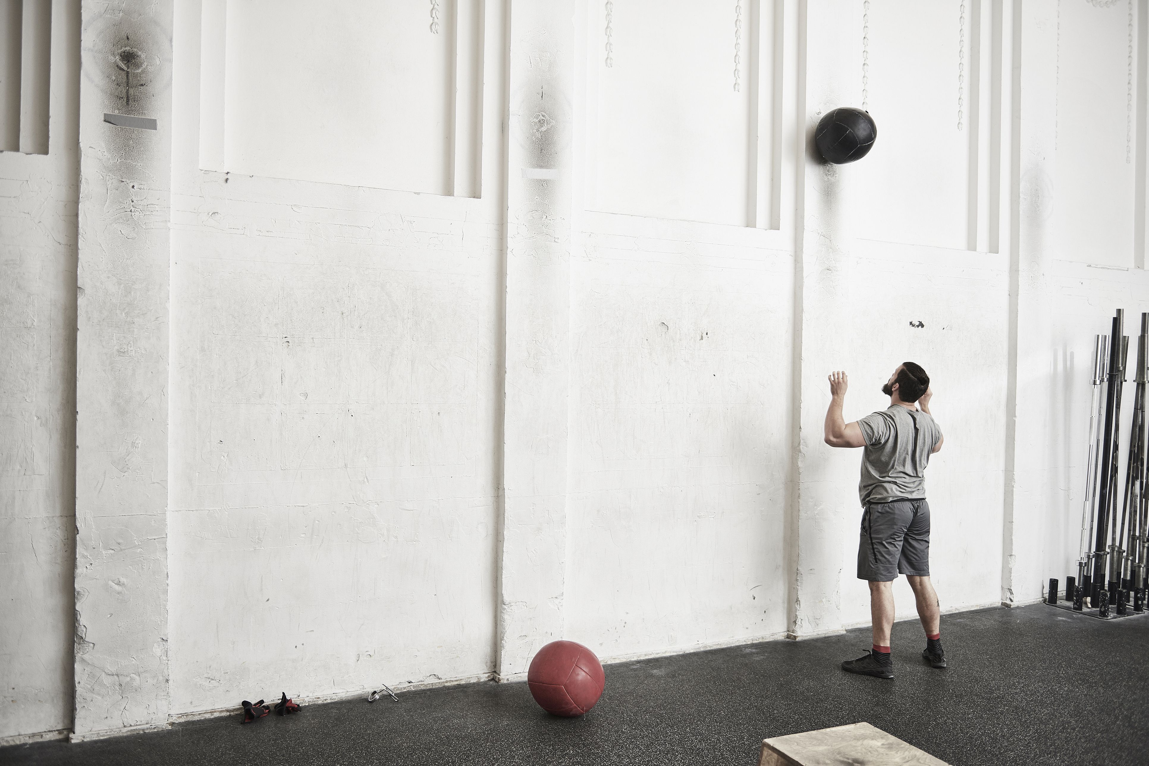Man throwing fitness ball against wall in cross training gym