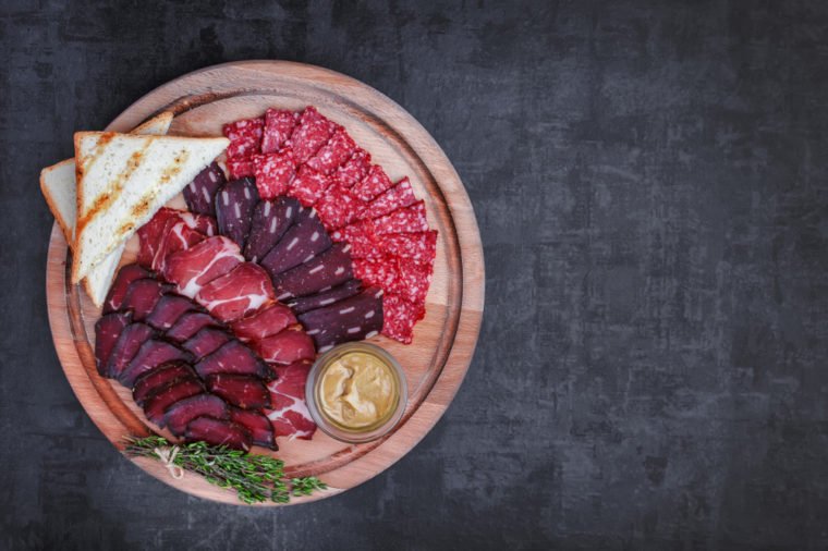 Salami, sliced ham, sausage, prosciutto, bacon. Meat antipasto platter on stone table. Top view with copy space