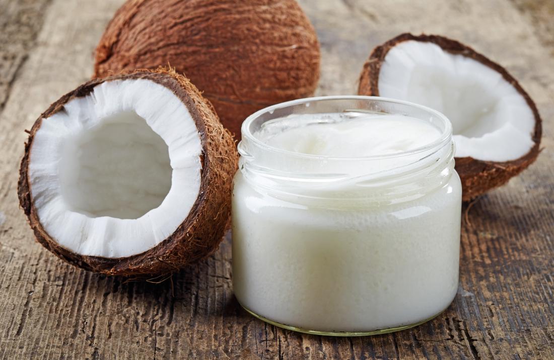 Coconut oil with halved coconut and oil in a jar on wooden table