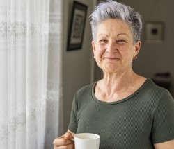 woman with Alzheimer's or a related dementia standing by window with coffee cup