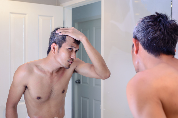 Man worried about gray hair looking into mirror