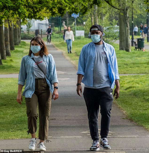 Two people are pictured wearing masks on London's Clapham Common on Sunday. Ministers could make a decision this week on whether to order the use of protective equipment for millions of Britons in the workplace and on public transport