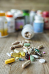 Many nutritional health supplements and vitamins in capsules, tablets on a wood background with their bottles in the background, shallow depth of focus.